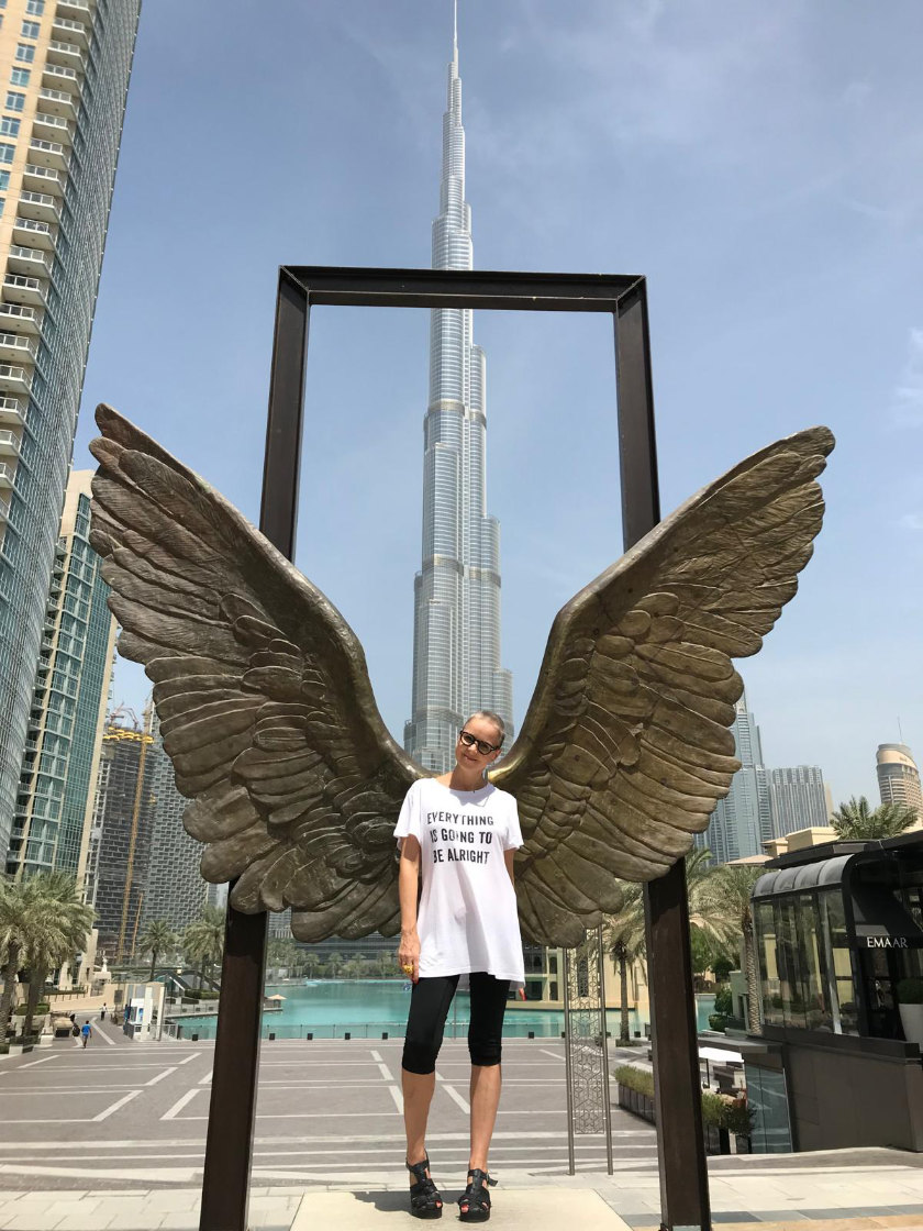 Mandi Kingsbury wearing a T-shirt with the words 'Everything's going to be alright' posing with large wings in front of the Burj Khalifa