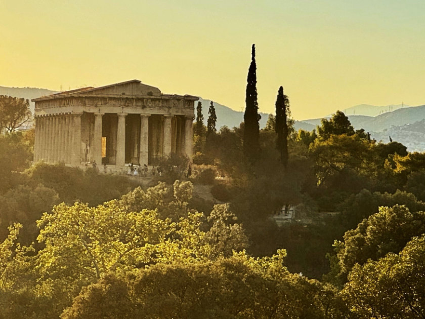 The Temple of Hephæstus. Pillared structure at left of image, surrounded by trees.