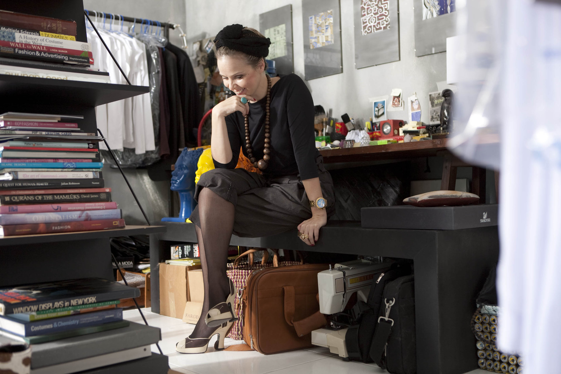 Mandi Kingsbury, photographed by Charney Magri. Image shows Mandi in black seated at a work table with creative books in the foreground.